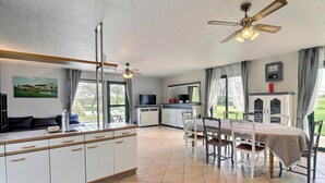 A modern kitchen with a dining area, large windows, and a ceiling fan.