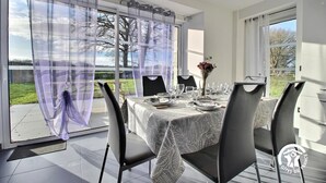 Un comedor con una mesa preparada para cuatro personas, ventanas amplias con cortinas translúcidas y vistas al exterior.