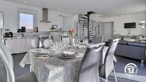 Un comedor moderno con una escalera en espiral, una cocina y un salón con sofá y televisor.