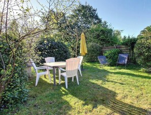 Um jardim com mesa e cadeiras, um guarda-sol amarelo e uma cerca de madeira.