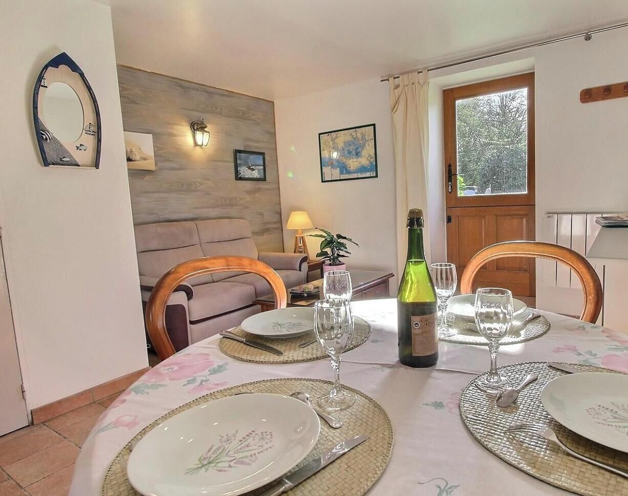 A dining area with a table set for two, a bottle of wine, and two glasses. There is a sofa and a lamp in the background.