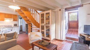 Ein geräumiger Wohnbereich mit einer Holztreppe, einem Esstisch mit Stühlen, einem Sofa und einem Fernseher auf einem Schrank.