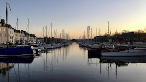 Un puerto deportivo con varias embarcaciones amarradas a lo largo de una vía fluvial tranquila, rodeado de edificios.