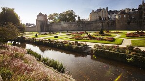 Un castillo histórico con un foso, jardines formales y una muralla de piedra.
