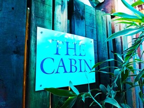 A sign that reads "THE CABIN" mounted on a wooden fence. - Boathouse Bed and Biscuit - Cabin (Margate)