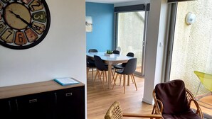 Ein modernes Wohnzimmer mit einer runden Wanduhr, einem Essbereich mit Tisch und Stühlen sowie einem Korbsessel.