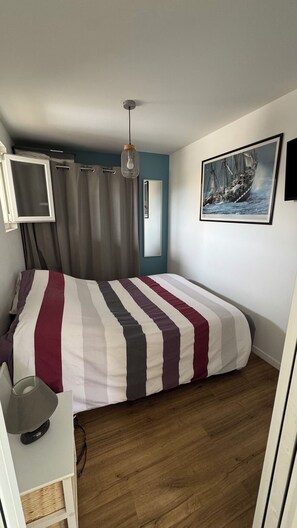 A bedroom with a bed, a desk, a chair, a TV, a mirror, and a painting on the wall.