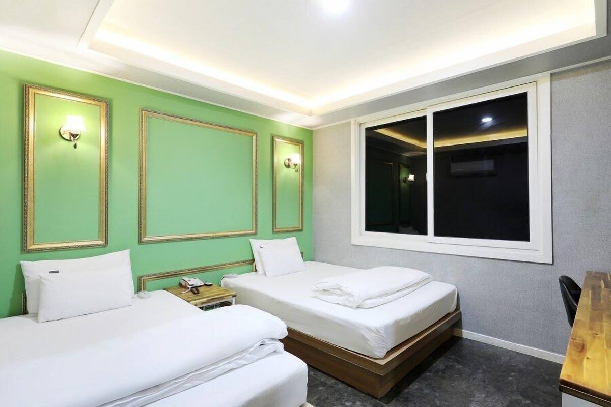 A hotel room with two beds, a desk, and a large window.