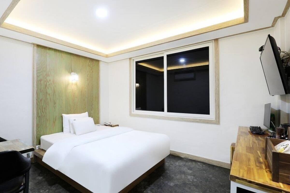 A hotel room with a bed, a desk, a chair, a TV, and a window.