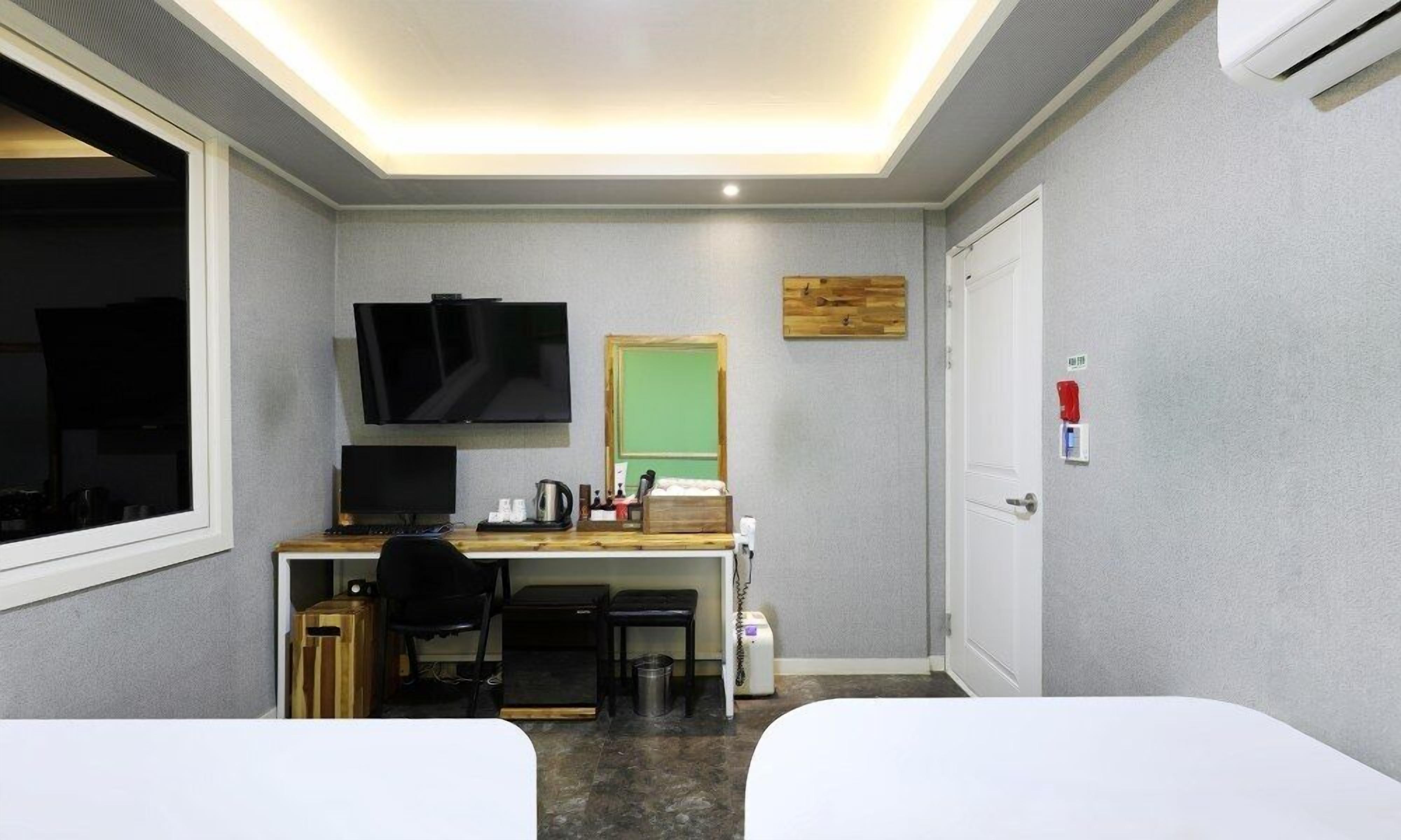 Habitación de hotel con escritorio, dos camas, televisor, espejo y aire acondicionado.
