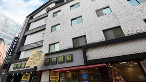 Een hotel met een moderne gevel, meerdere ramen en een bord dat een feestelijke opening aangeeft.