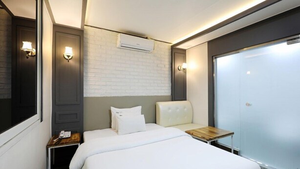 Een hotelkamer met een bed, nachtkastje, stoel, garderobe en een airconditioningsysteem.
