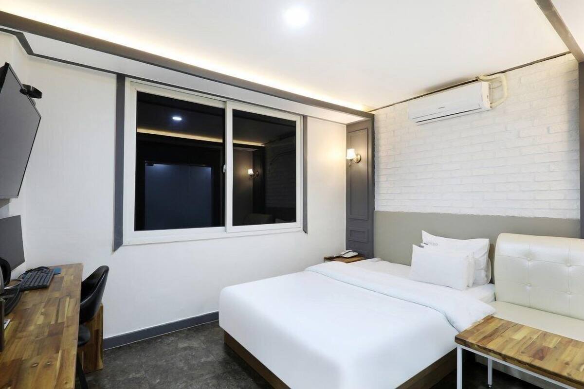A hotel room with a bed, a desk, a chair, a TV, and a window.