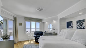 Une chambre à coucher avec un grand lit, une chaise, une commode, un miroir et une vue sur l’océan.