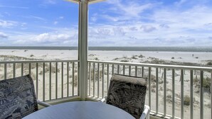 Vue sur la plage depuis un balcon couvert, doté de balustrades blanches et de coussins à motifs.