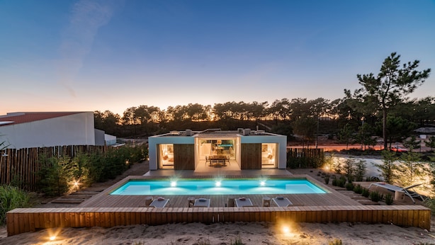 A modern outdoor pool area with a wooden deck, lounge chairs, and a dining area with a table and chairs.