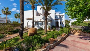 A white villa with a tiled roof, surrounded by palm trees and potted plants.