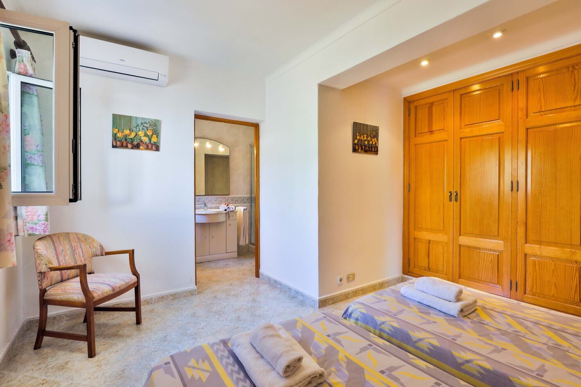 Une chambre à coucher avec un lit, une chaise, une armoire et une salle de bain visible à travers une porte ouverte.