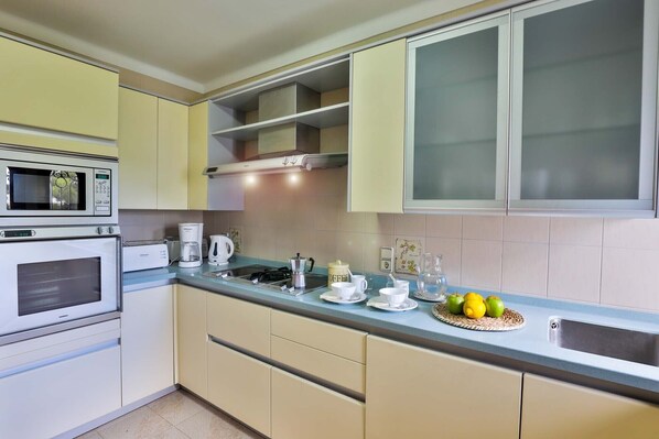 A kitchen with a microwave, oven, coffee maker, and a fruit bowl on the counter.