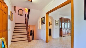 A spacious hallway with a wooden staircase, a cabinet, and wall-mounted lights.