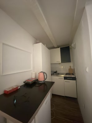 A compact kitchen with white cabinets, a black countertop, a pink kettle, and a pair of glasses on the counter. - Apartment in Center Old Town (Dubrovnik)