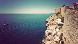 A coastal view with a stone wall and a sailboat on the water. - Apartment in Center Old Town (Dubrovnik)