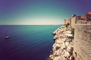 A coastal view with a stone wall and a sailboat on the water.