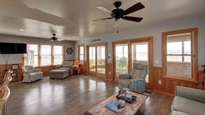 A spacious living room with a ceiling fan, large windows, and a view of the outdoors. - Shore Enuf - Ocracoke Island (Ocracoke)