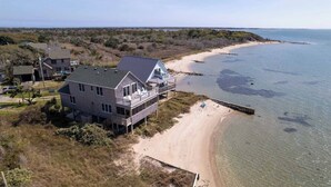 A beachfront property with a large house featuring a balcony, a pier extending into the water, and a sandy beach. - Shore Enuf - Ocracoke Island (Ocracoke)