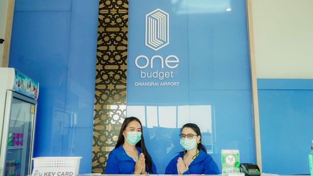 Mostrador de recepción en One Budget Chiangrai Airport, con una pared azul y un logotipo.