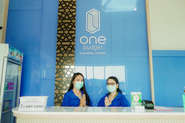 Mostrador de recepción en One Budget Chiangrai Airport, con una pared azul y un logotipo.