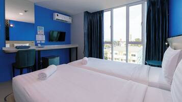 A hotel room with two beds, a desk, a chair, a TV, and a large window with curtains.