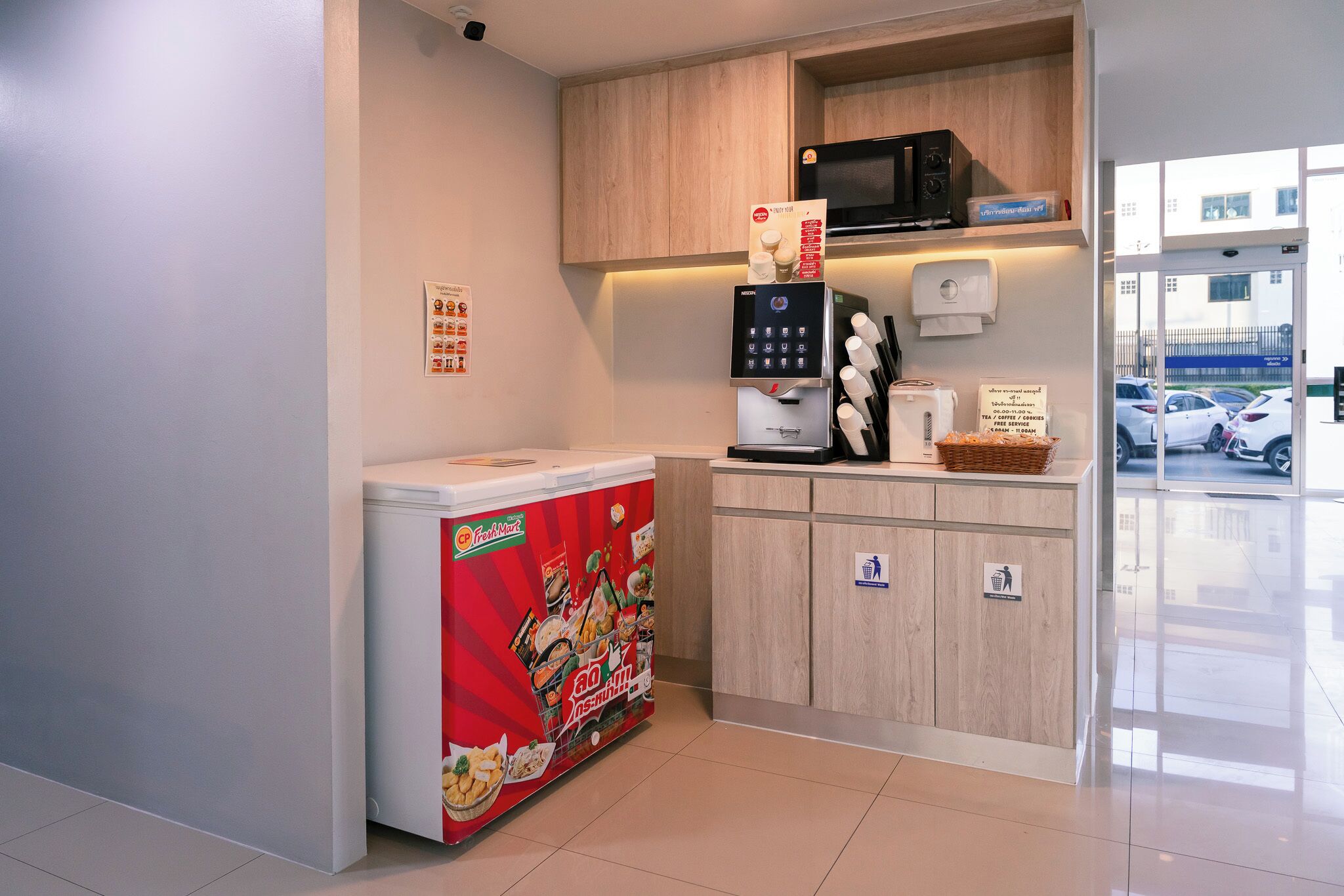 A kitchenette with a refrigerator, microwave, coffee maker, and a trash bin.