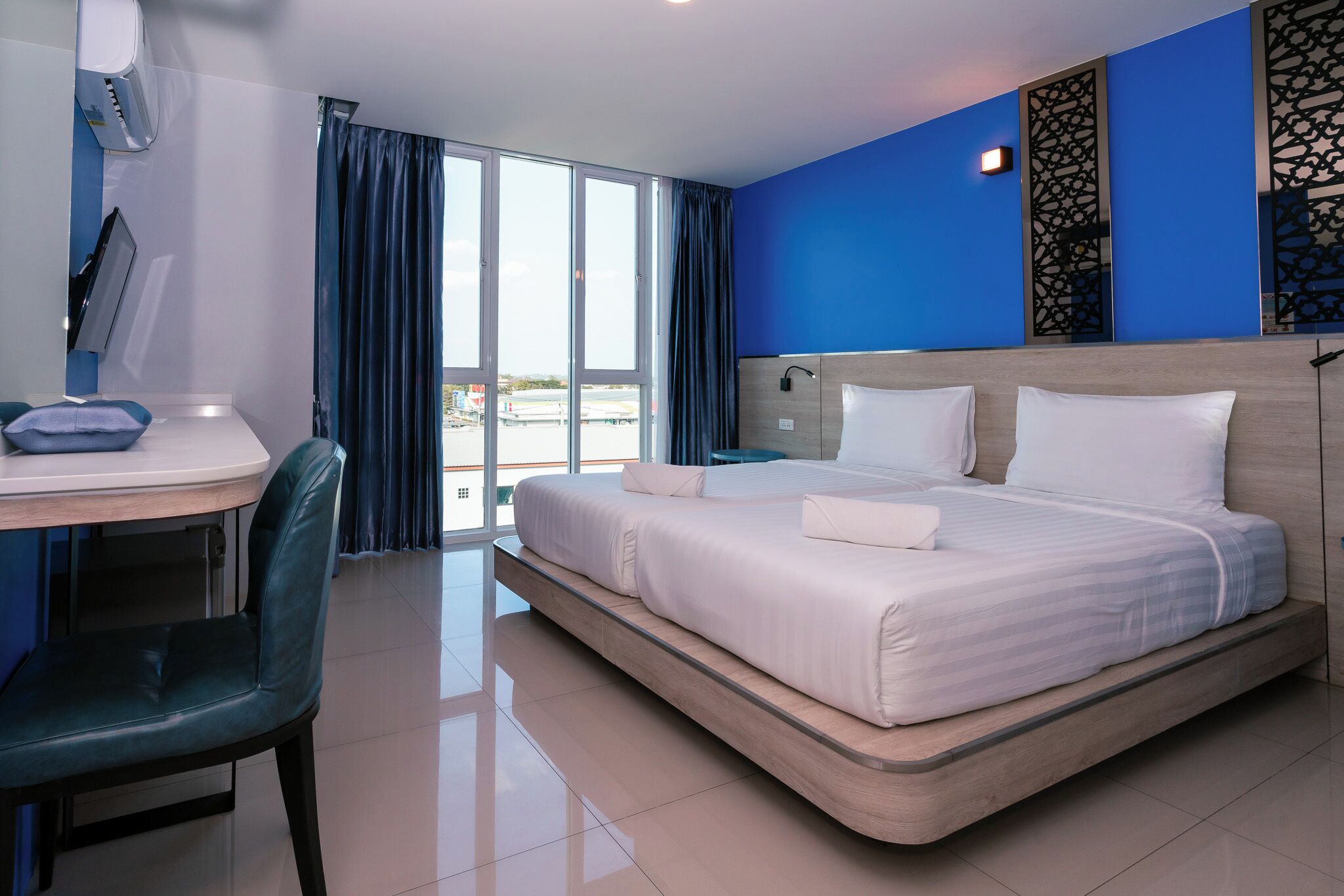 Habitación de hotel con cama, escritorio, silla y vistas amplias por un ventanal.