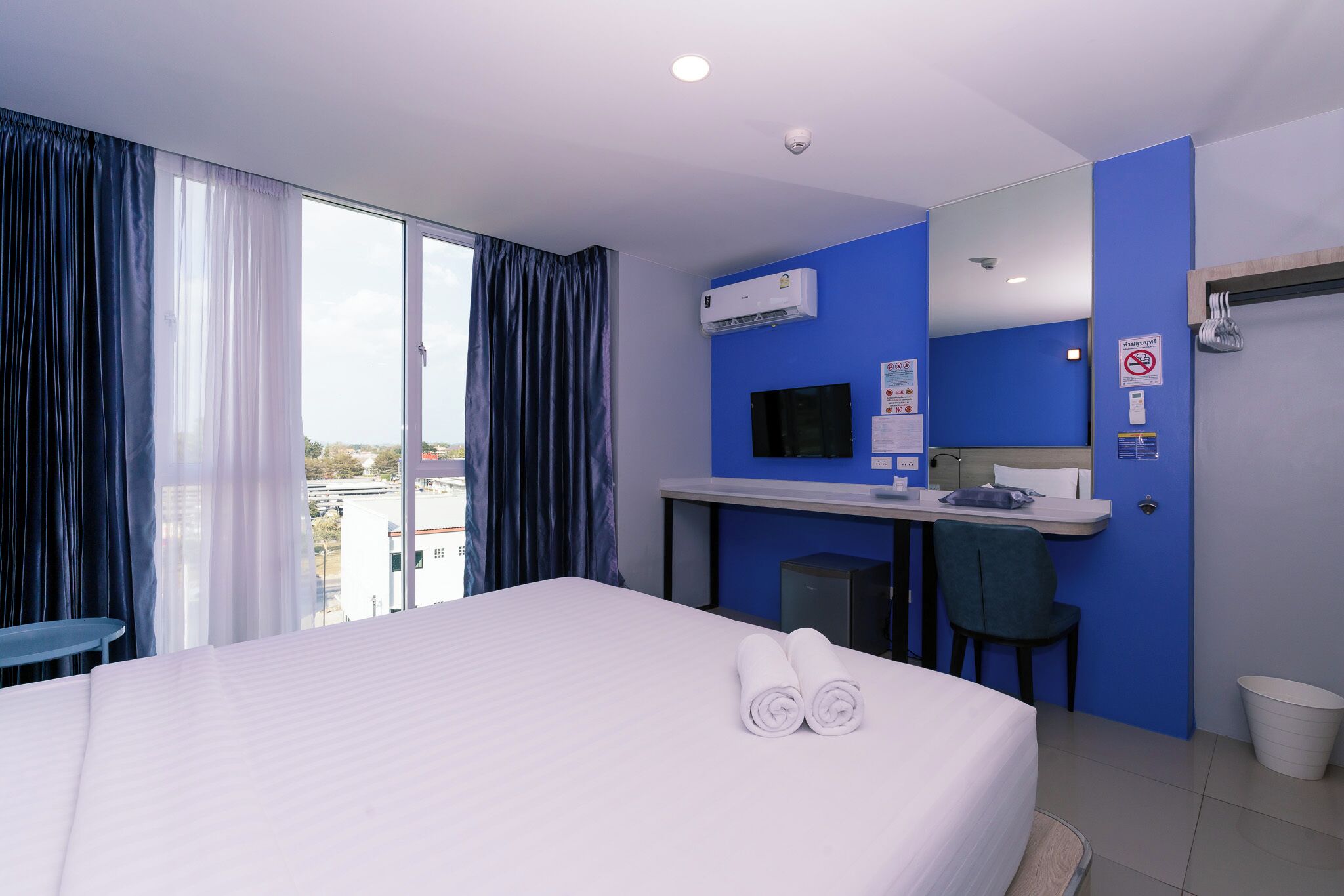 A hotel room with a bed, a desk, a chair, a TV, and a window with curtains.