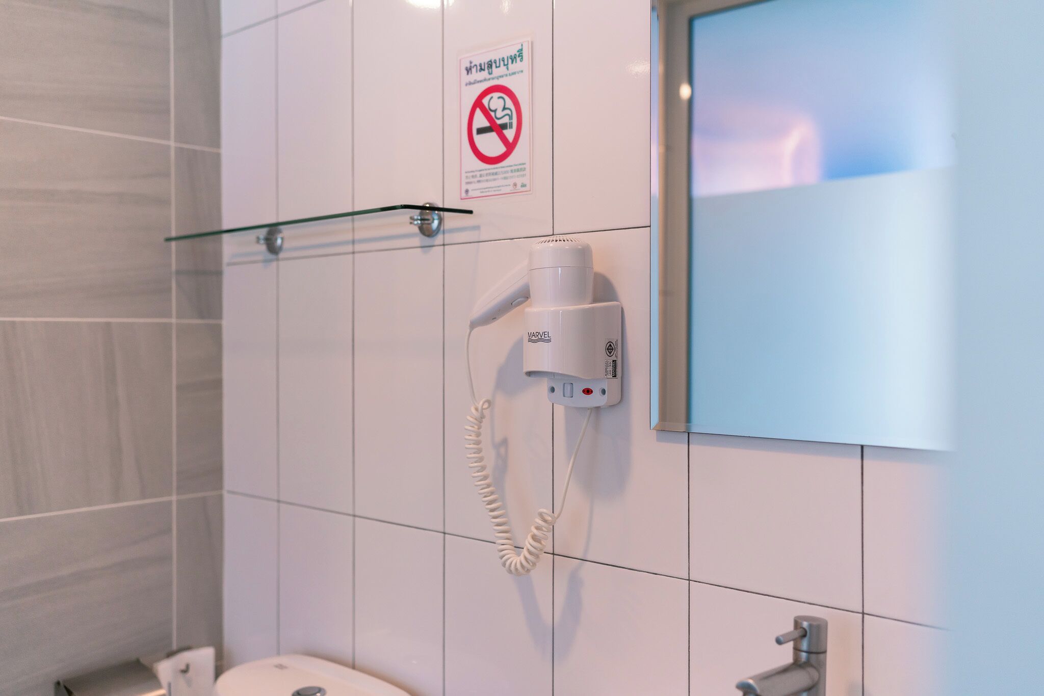 A bathroom with a hand dryer, a no-smoking sign, and a glass shelf.