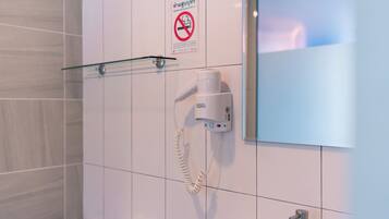 A bathroom with a hand dryer, a no-smoking sign, and a glass shelf.