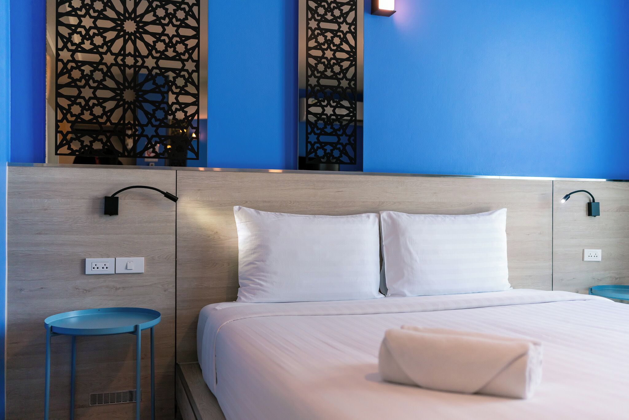 A hotel room with a bed, a nightstand, a wall-mounted lamp, and a decorative panel.