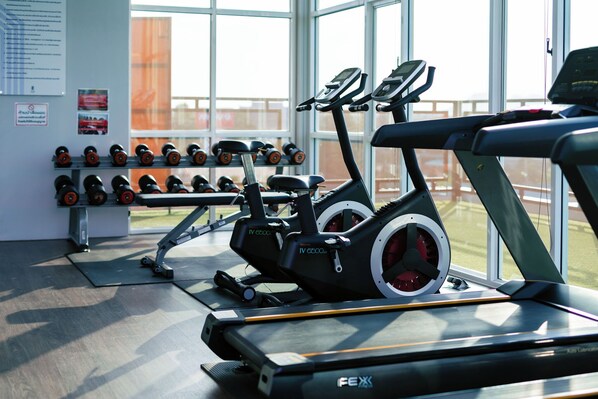 Un gimnasio con equipo de cardio, mancuernas y cinta de correr.