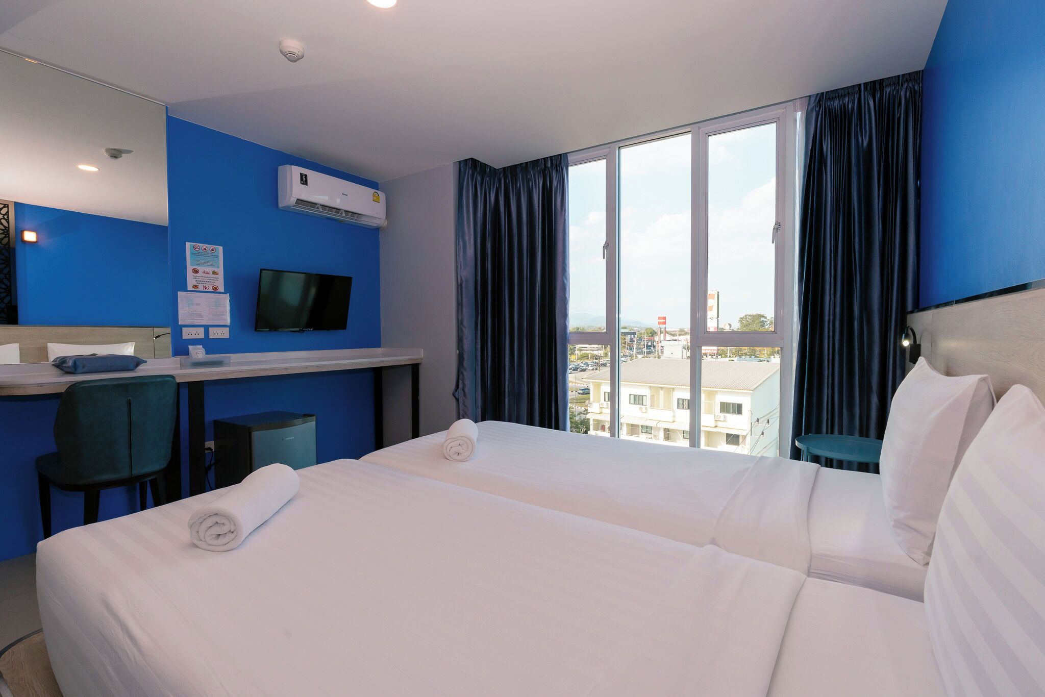 Una habitación de hotel con cama, escritorio con computadora, televisor y ventana con cortinas.