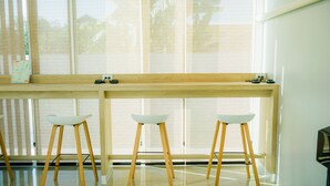 Una habitación moderna con un amplio ventanal, un escritorio de madera y tres taburetes blancos.