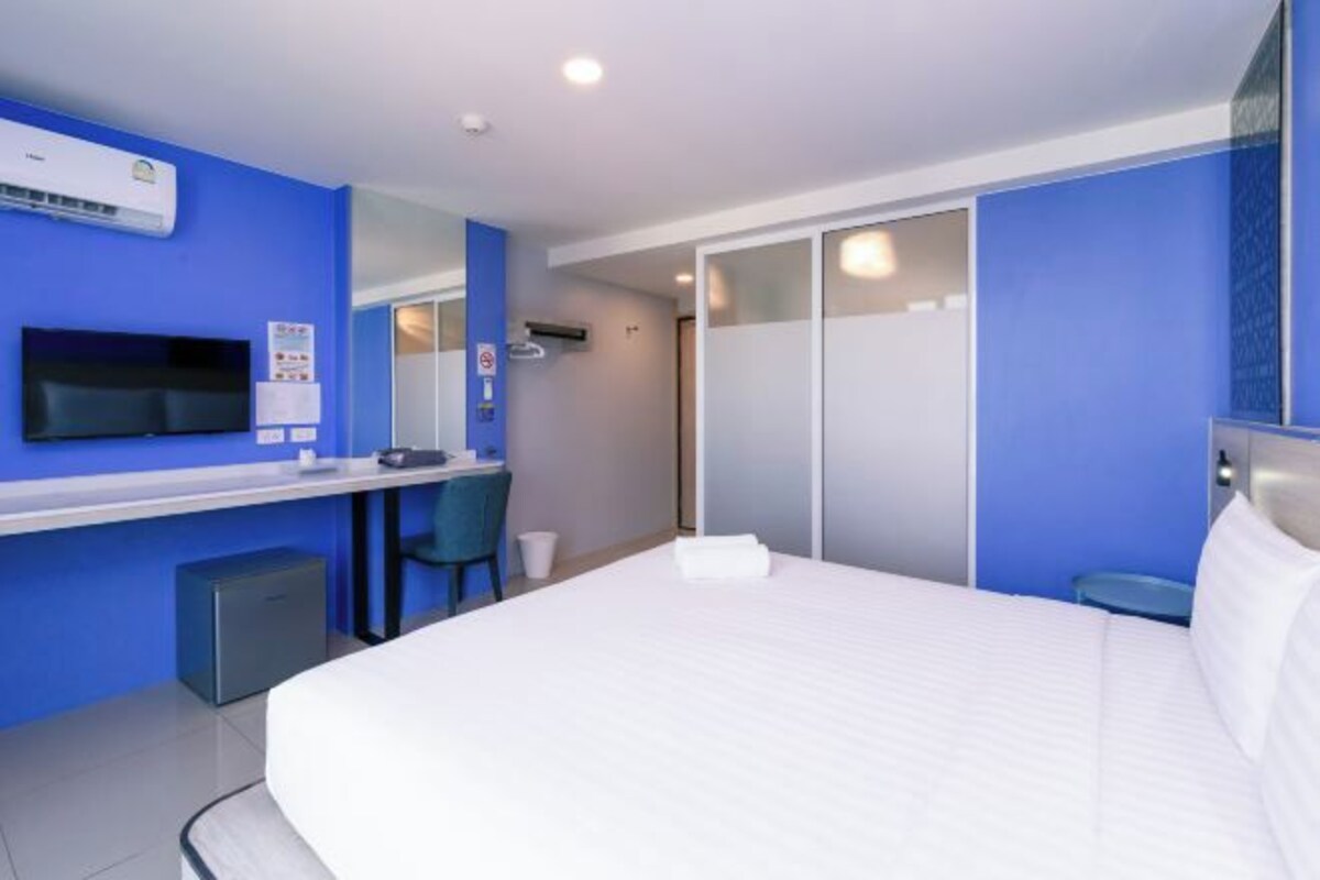 A hotel room with a bed, a desk, a chair, a television, and a sliding door.