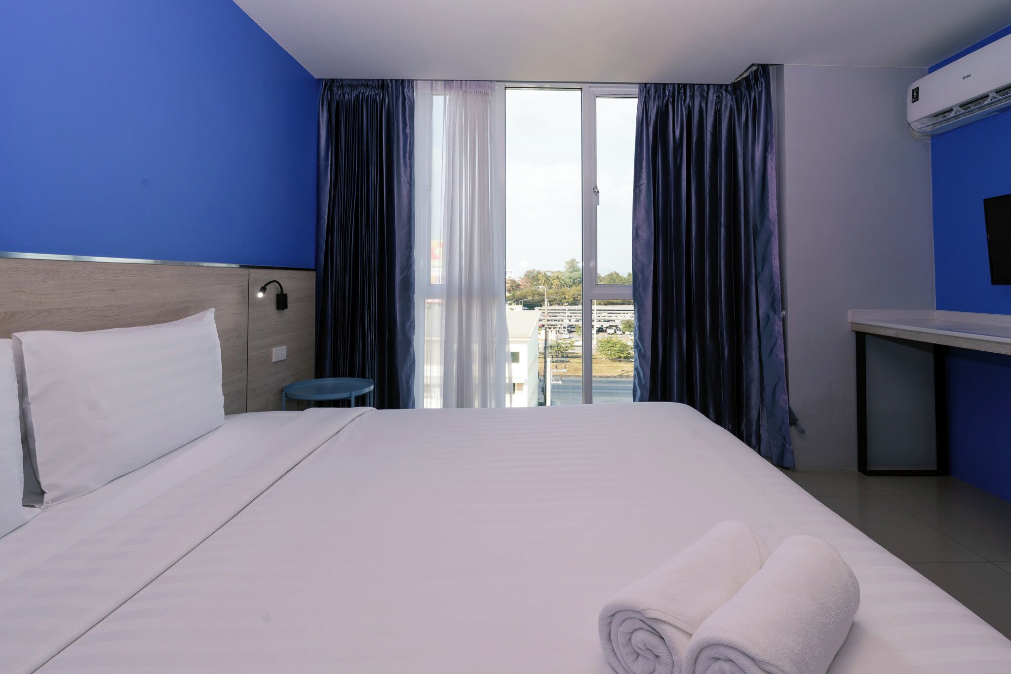 A hotel room with a large bed, a desk, a chair, and a view of the outdoors.