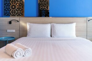 Habitación de hotel con cama, dos almohadas, mesita de noche, lámpara y pared con paneles decorativos.