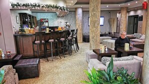 Un vestíbulo de hotel con una zona de bar, diferentes disposiciones de asientos y un pilar grande.