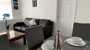 A modern living room with a brown leather sofa, a dining table set with white plates, bowls, and a silver vase. - Large 5 Bed House / Wolverhampton + Parking (Wolverhampton)