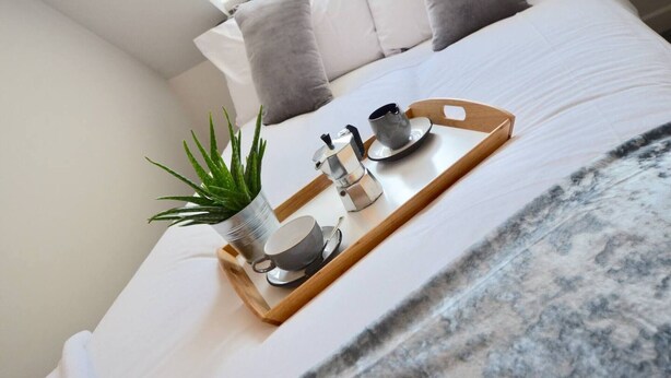 A neatly made bed with a tray containing a plant, a coffee maker, and a cup and saucer. - Large 5 Bed House / Wolverhampton + Parking (Wolverhampton)