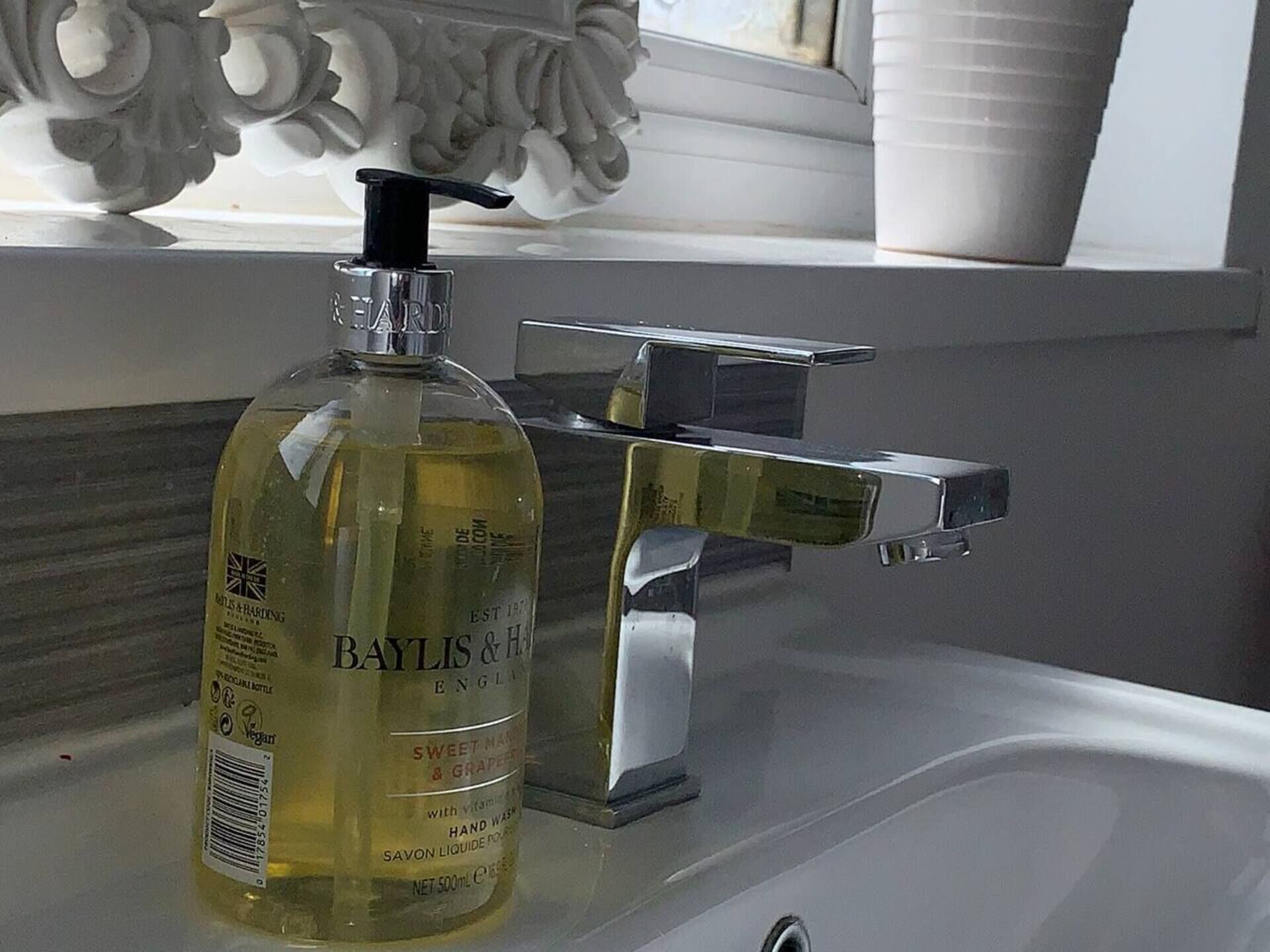 A Baylis & Hardings sweet mango and grape hand wash bottle on a bathroom sink with a modern faucet.
