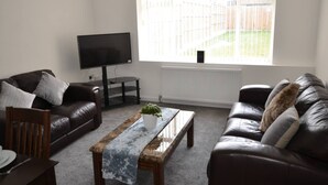 A living room with a flat-screen TV, two leather sofas, a coffee table, and a window with a view of a backyard. - Large 5 Bed House / Wolverhampton + Parking (Wolverhampton)
