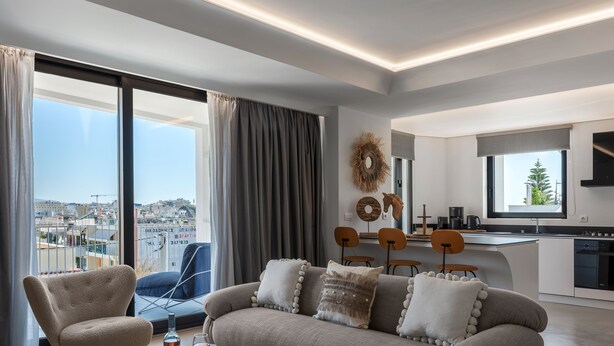 Una sala de estar moderna con un sofá, sillones y vistas a la ciudad a través de amplios ventanales.